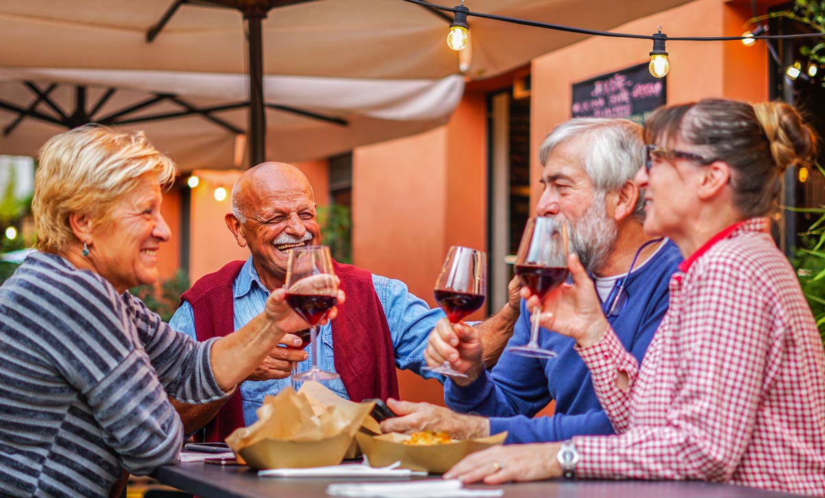 smiling and laughing group of four white male and female seniors enjoying wine together at a table outside