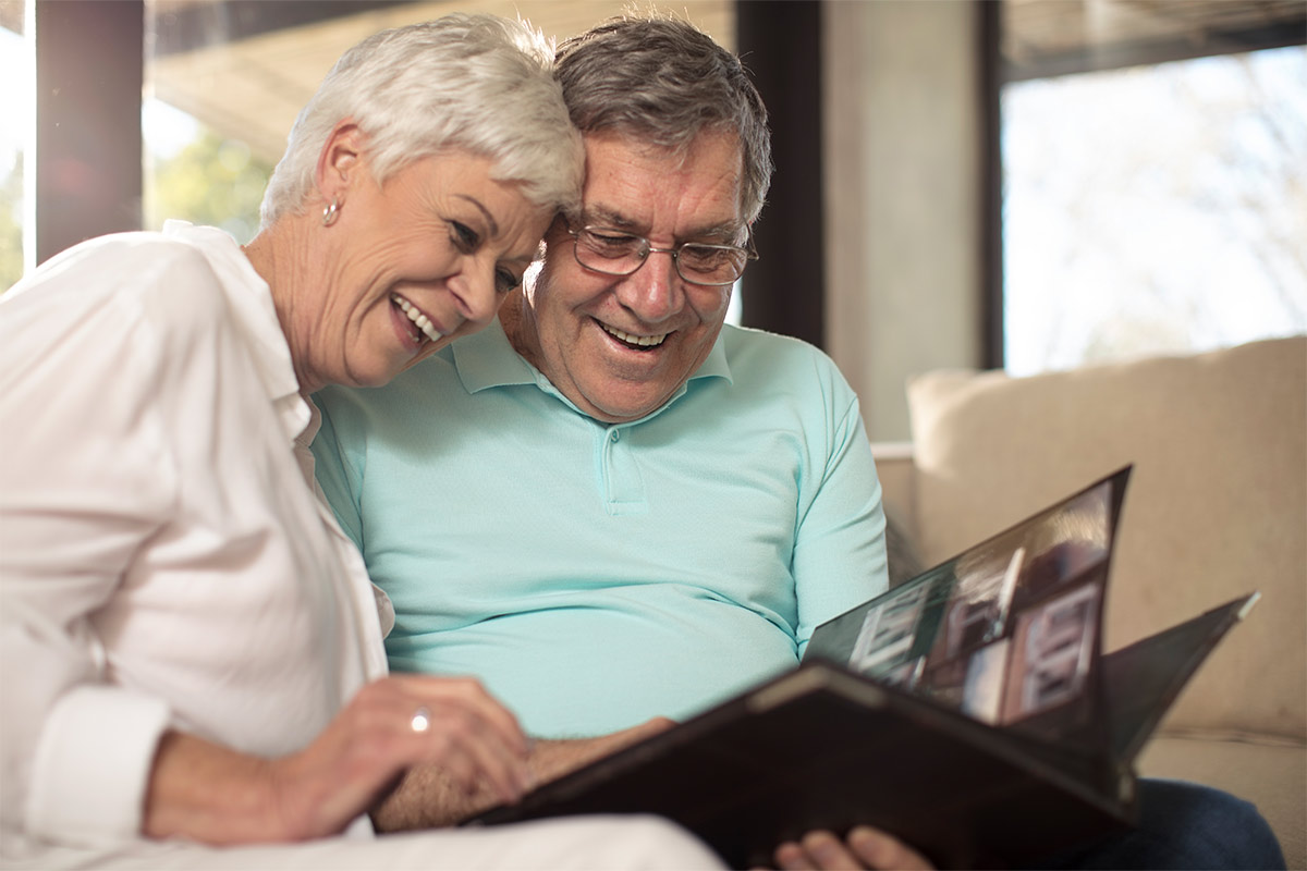 Elderly couple smiles and laughs while looking at a photo album together