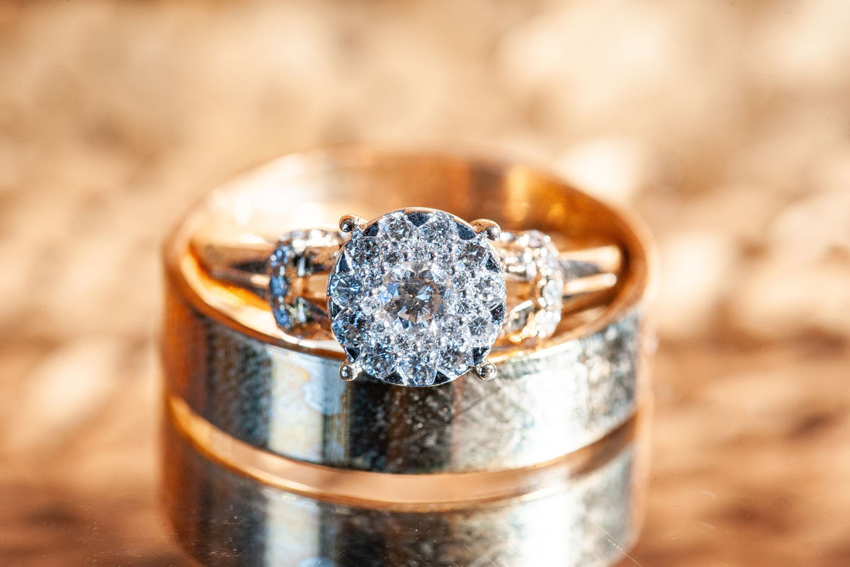 Diamond wedding ring resting inside a men’s charcoal and gold wedding band against a gold blurred background