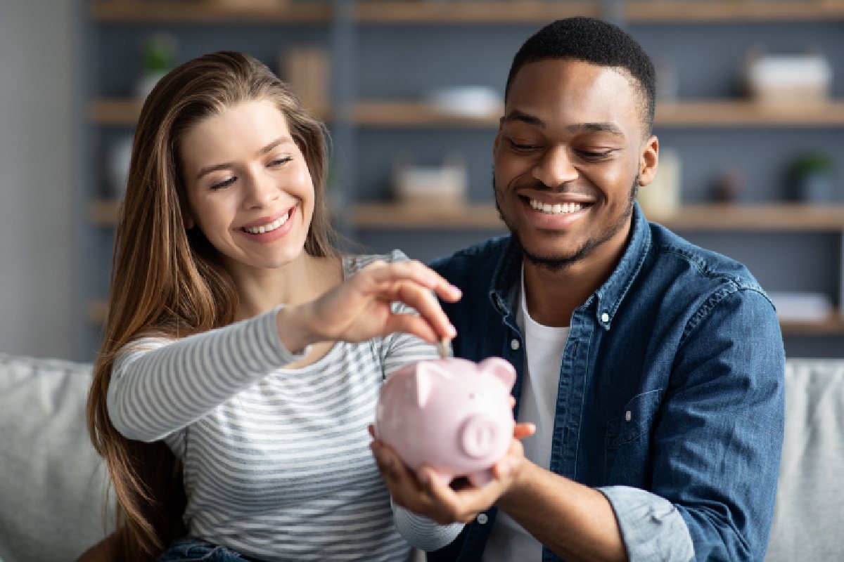 A white 20-something woman putting a coin in a piggy bank held by a black 20-something man