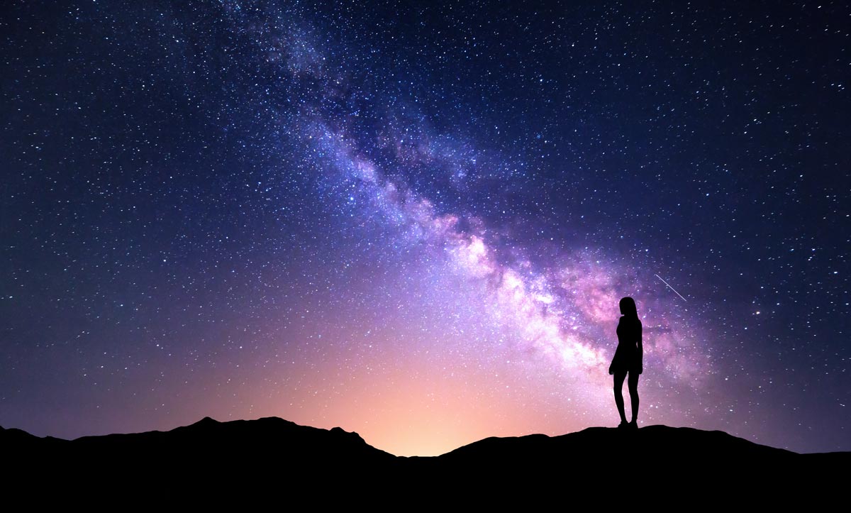 An outline of a woman standing outside watching the purple sky and stars