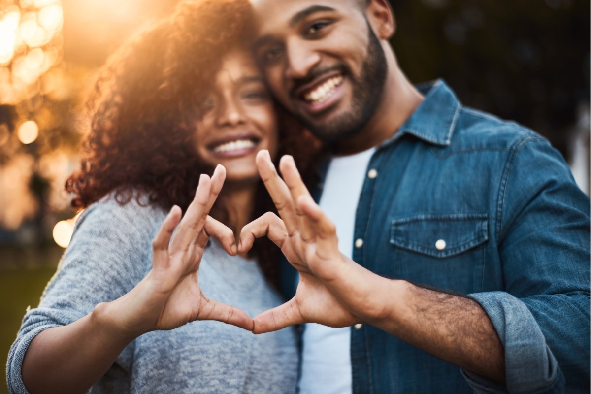 black 30-something couple making a heart with their hands with the sunset in the background with trees