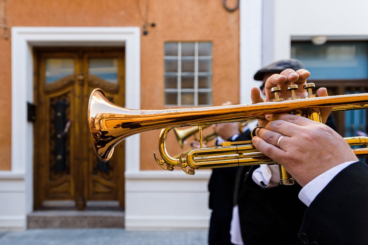 Close up of a white man holding and playing a trumpet outside with white male standing next to him