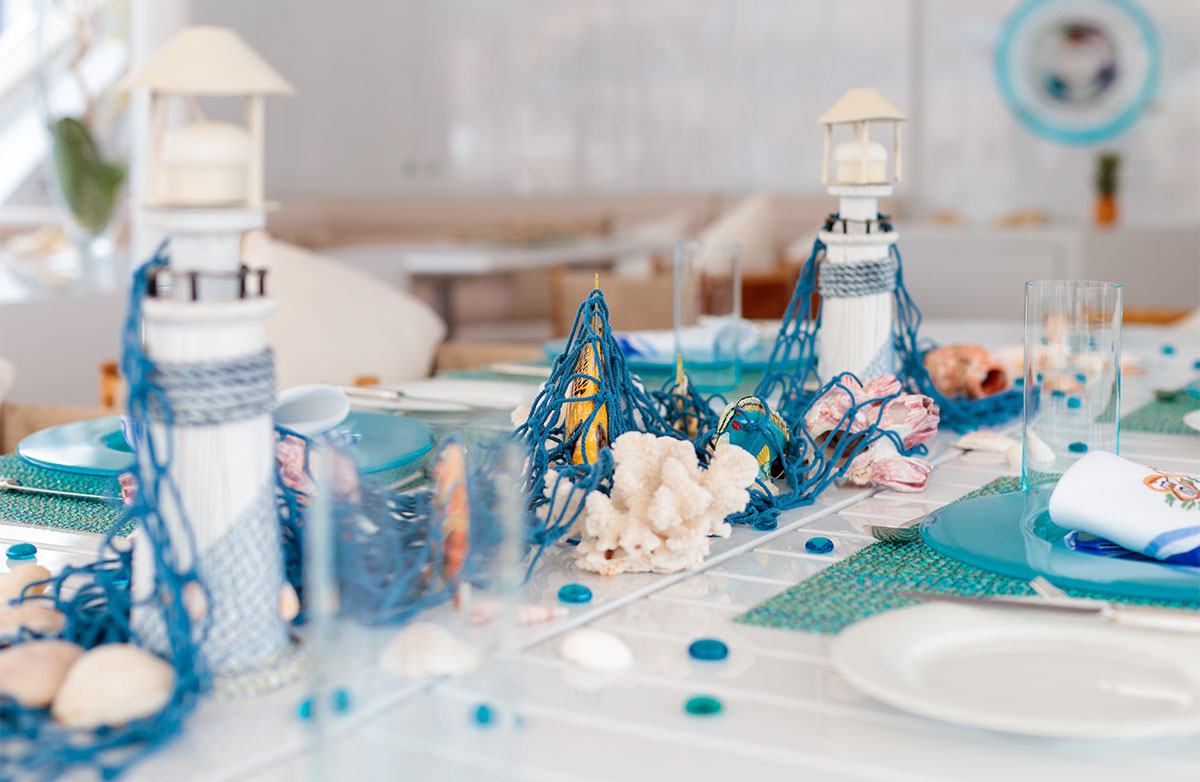 Little blue and white light houses, seashells, and blue fishing netting placed on a white table for decorations