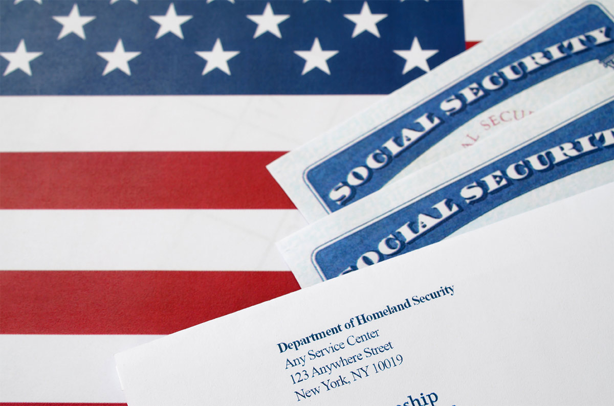 Two social security cards and an envelope from the Department of Homeland Security on an American flag background.