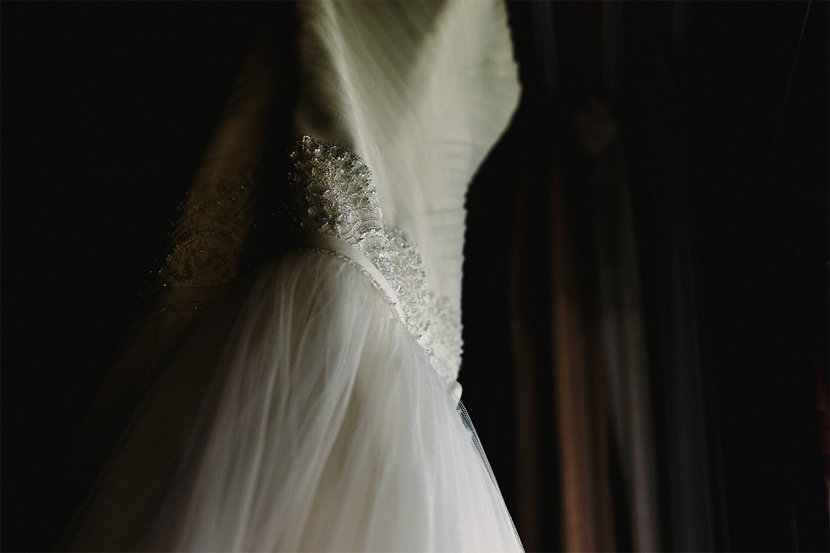 Close up of the waist of a wedding dress hanging in front of a dark background.