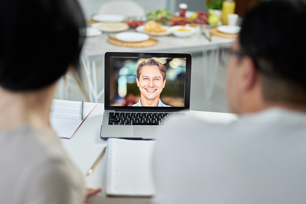 A focused picture of a 45-60 aged white man on a laptop screen video chatting with two people