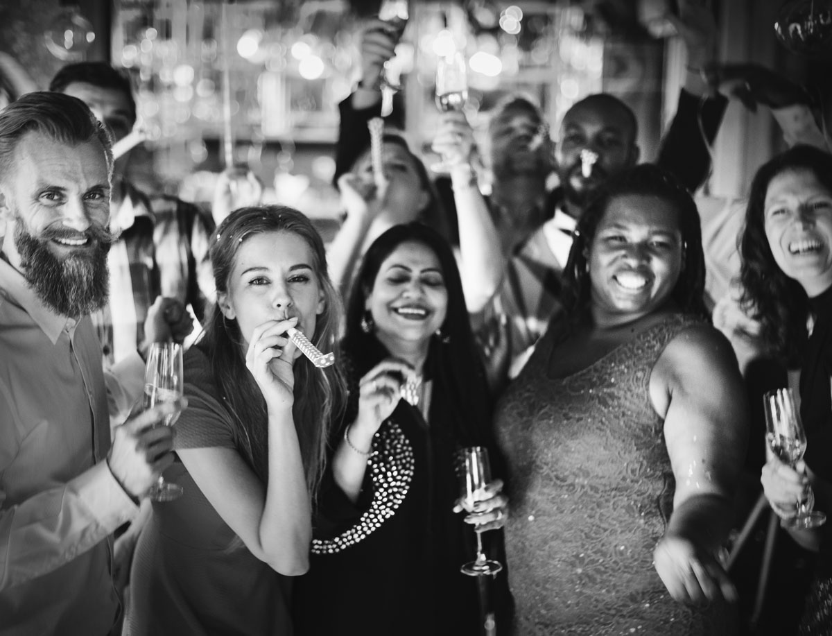 group of 40 something multiracial friends celebrating with noise makers and champagne flutes with black and white filter