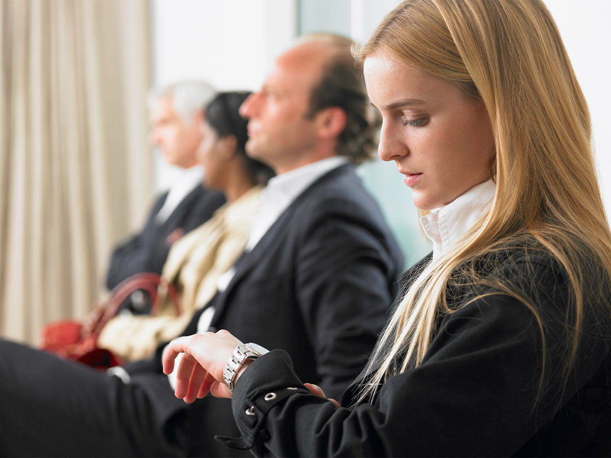 20-something white woman looking at her watch sitting in line in a business suit.