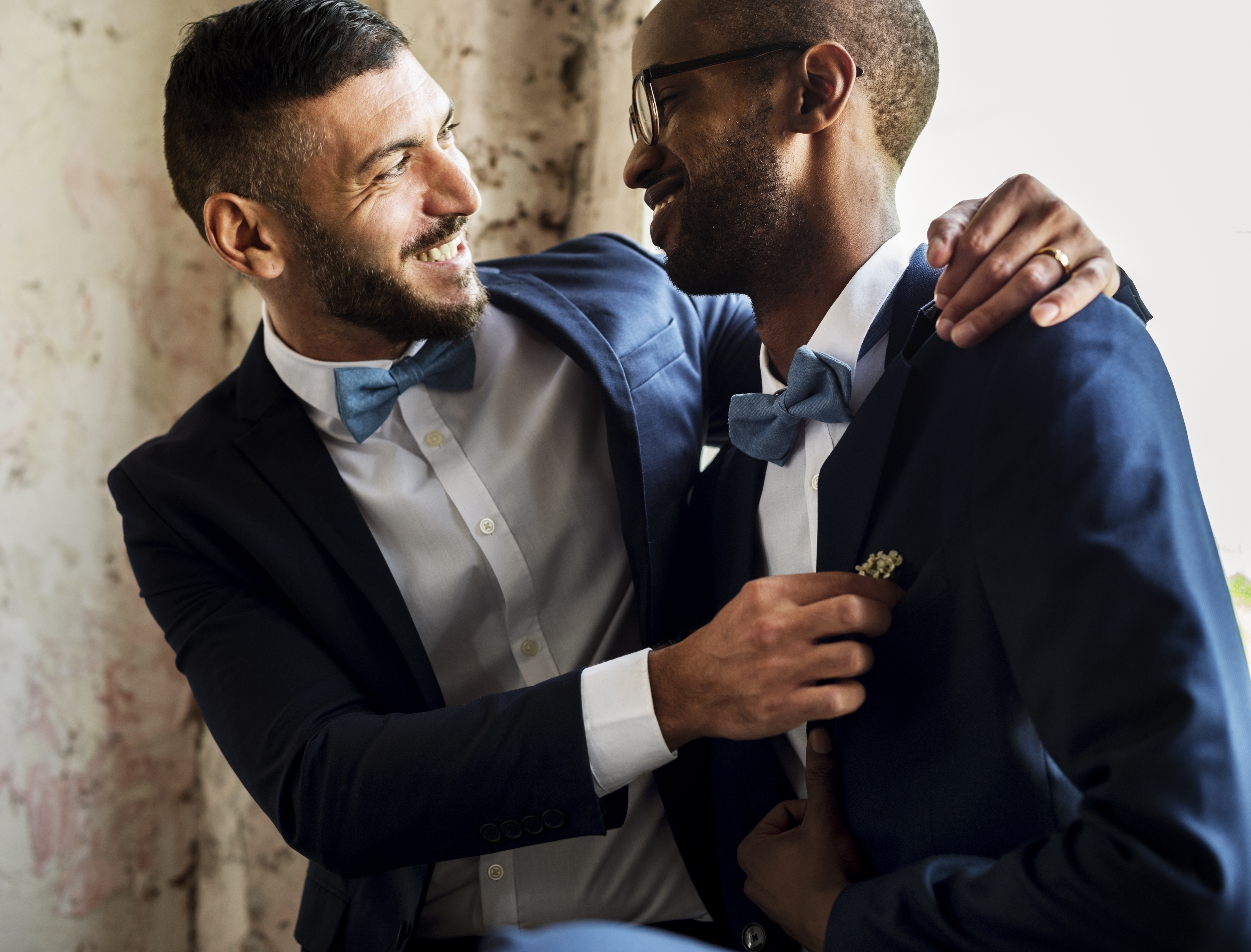  20 somethings Black and white men in suits laughing and looking at each other, while hugging. 