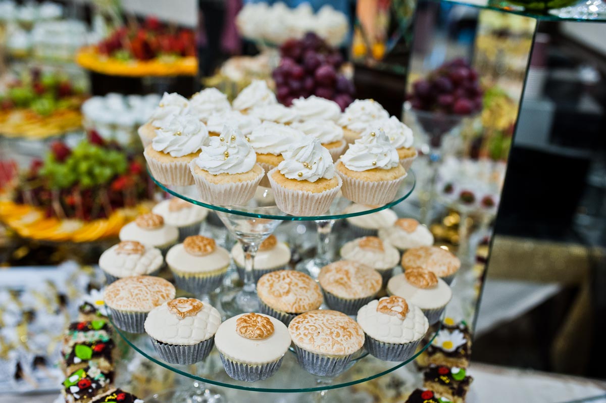 Focused shot of a tiered display of different flavors of white cupcakes at an event with blurred food dishes in the background