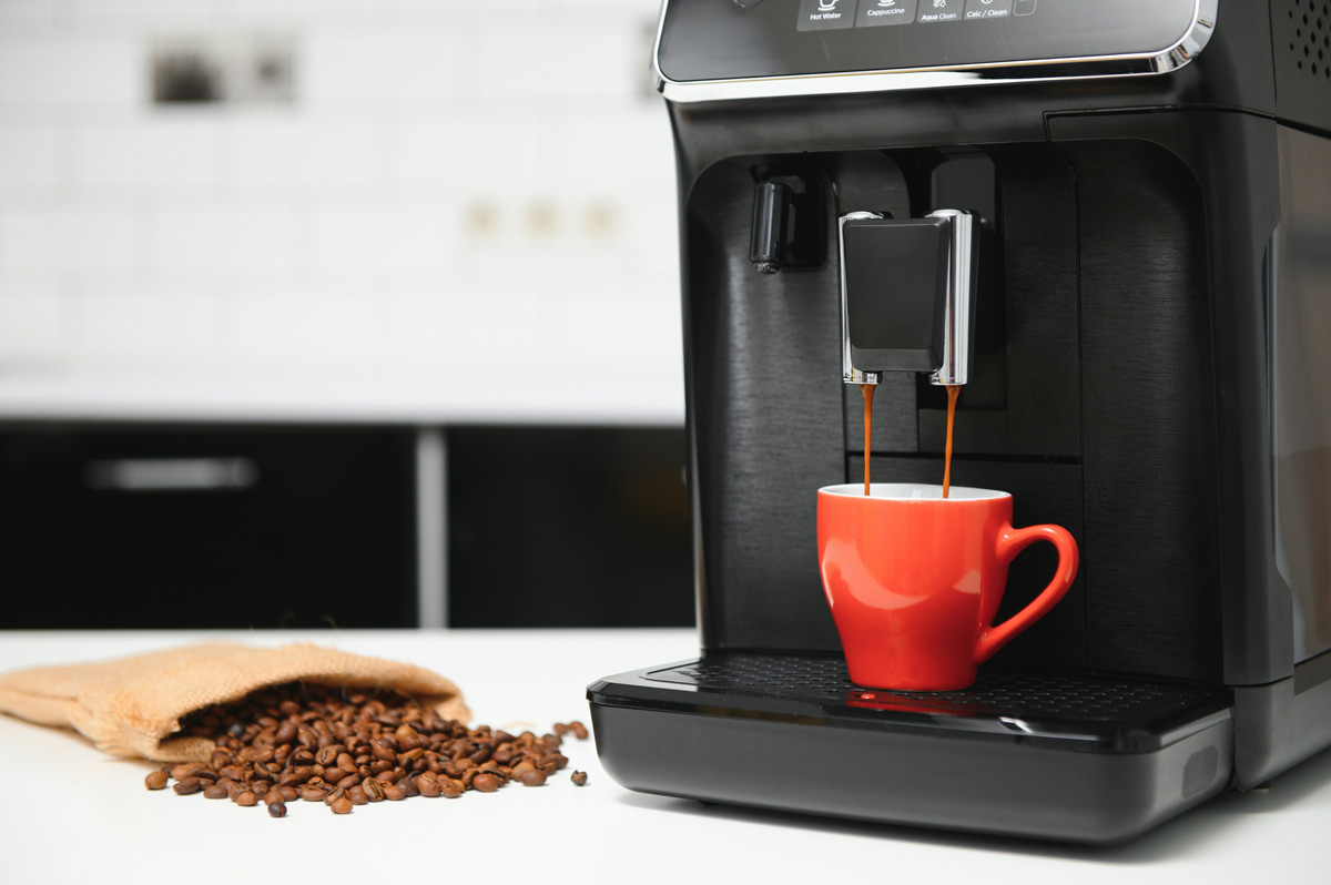 Coffee machine making coffee into a small red coffee cup next to a spilled pile of coffee beans on a white countertop