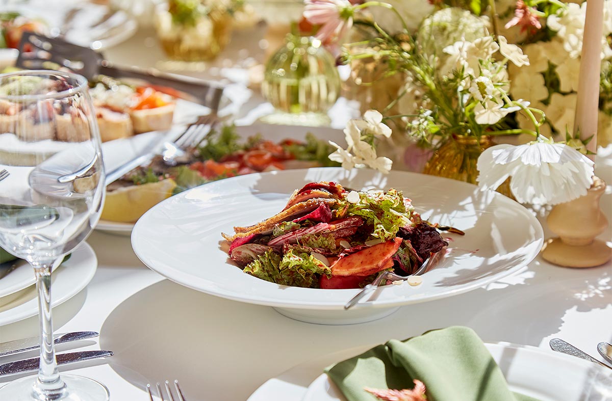 Expensive entree sits on a white table surrounded by glassware, other dishes, and floral centerpieces 