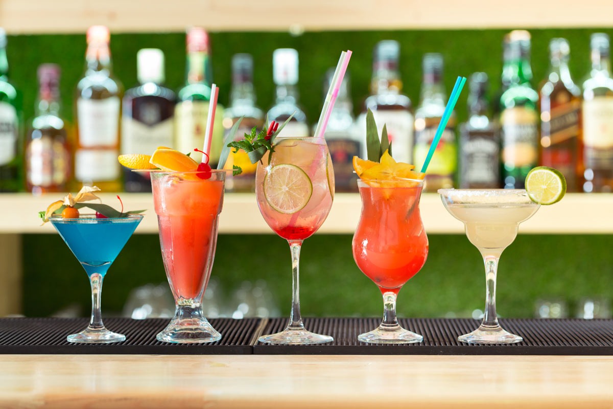 A vibrant array of 5 cocktails in various colors lined up on a polished bar, showcasing their enticing garnishes.