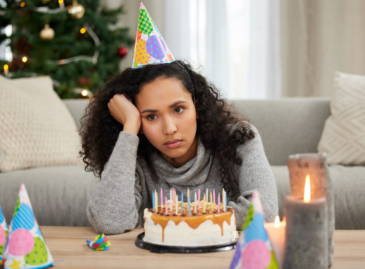 Mid 20’s black woman, sad sitting in front of cake without burning candles 