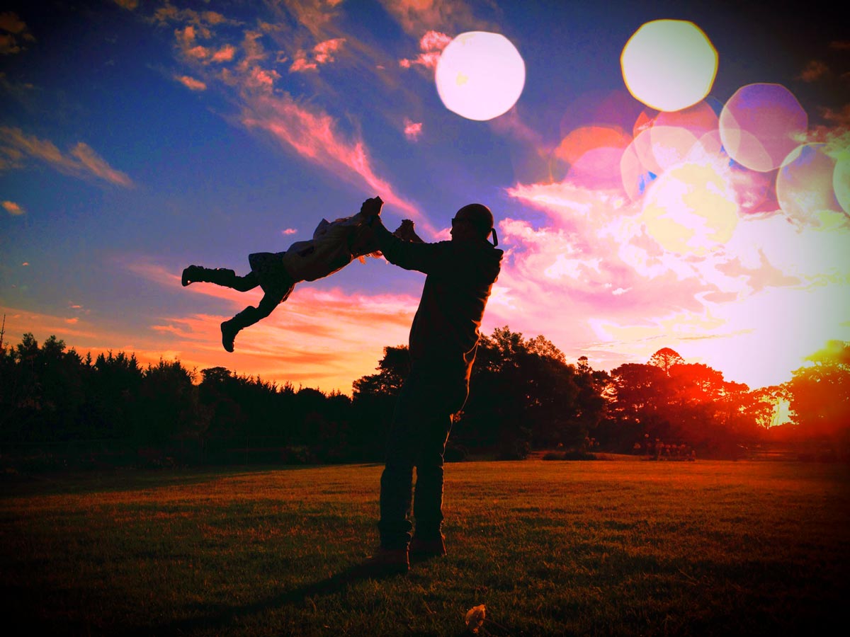  A grandpa swinging a little girl through the air as the sun is setting