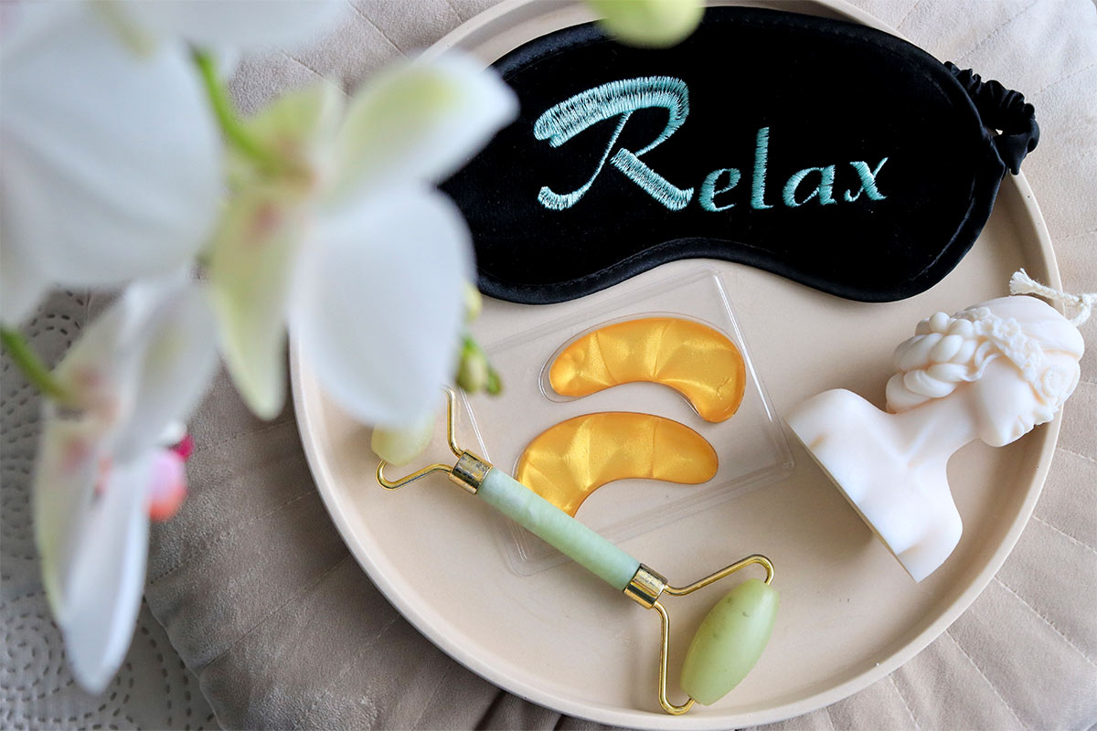 Relaxing spa scene with under eye mask, facial roller, and eye mask with the writing relax on a plate emphasizing self-care practices for pre-wedding relaxation.