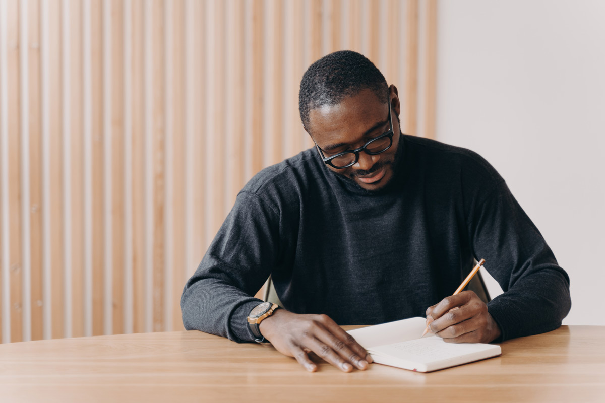 Black 35-year-old man wearing glasses writing his best man speech to the groom. 