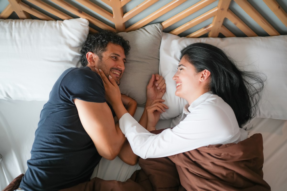 white 40-something couple in bed smiling and staring at each other