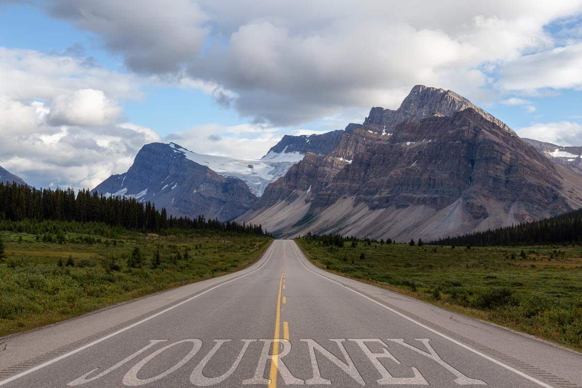 A view of distant mountains with trees and a street that says Journey 