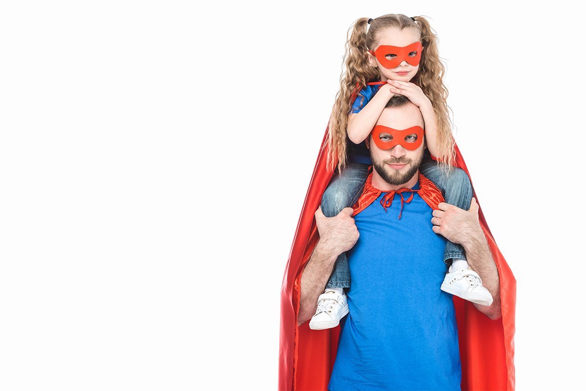 White father and 5-year-old daughter in matching blue shirts, red capes, and red masks with her on his shoulders